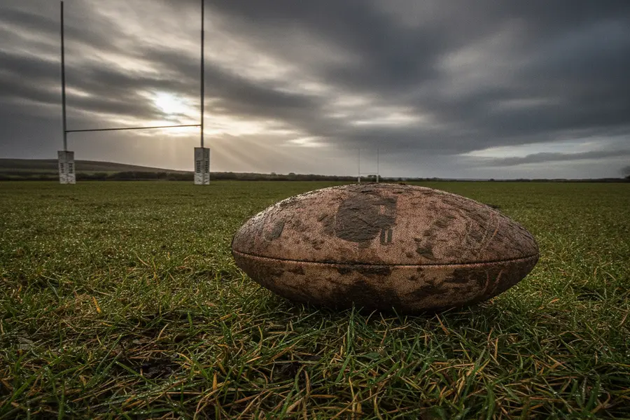 Muddy rugby match ball resting by the touchline bench